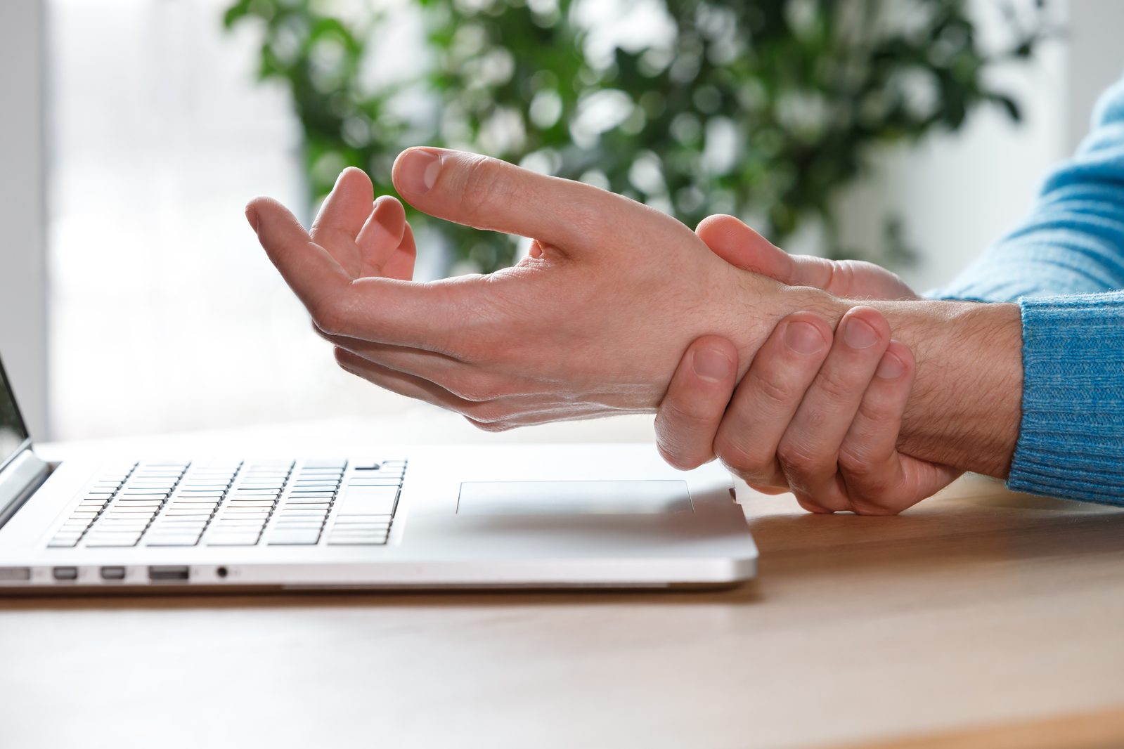 Person holding a painful wrist while working at a computer, a common presentation of carpal tunnel syndrome